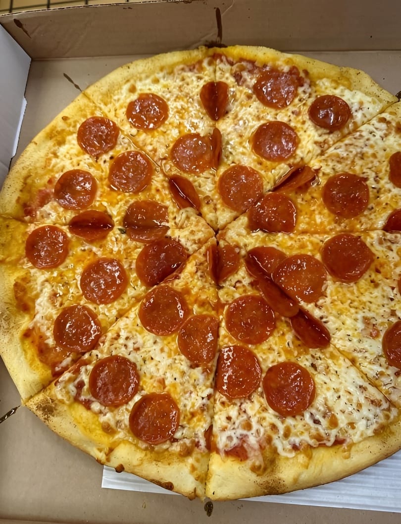 A whole pepperoni pizza with melted cheese and a golden crust, sliced and ready to eat.